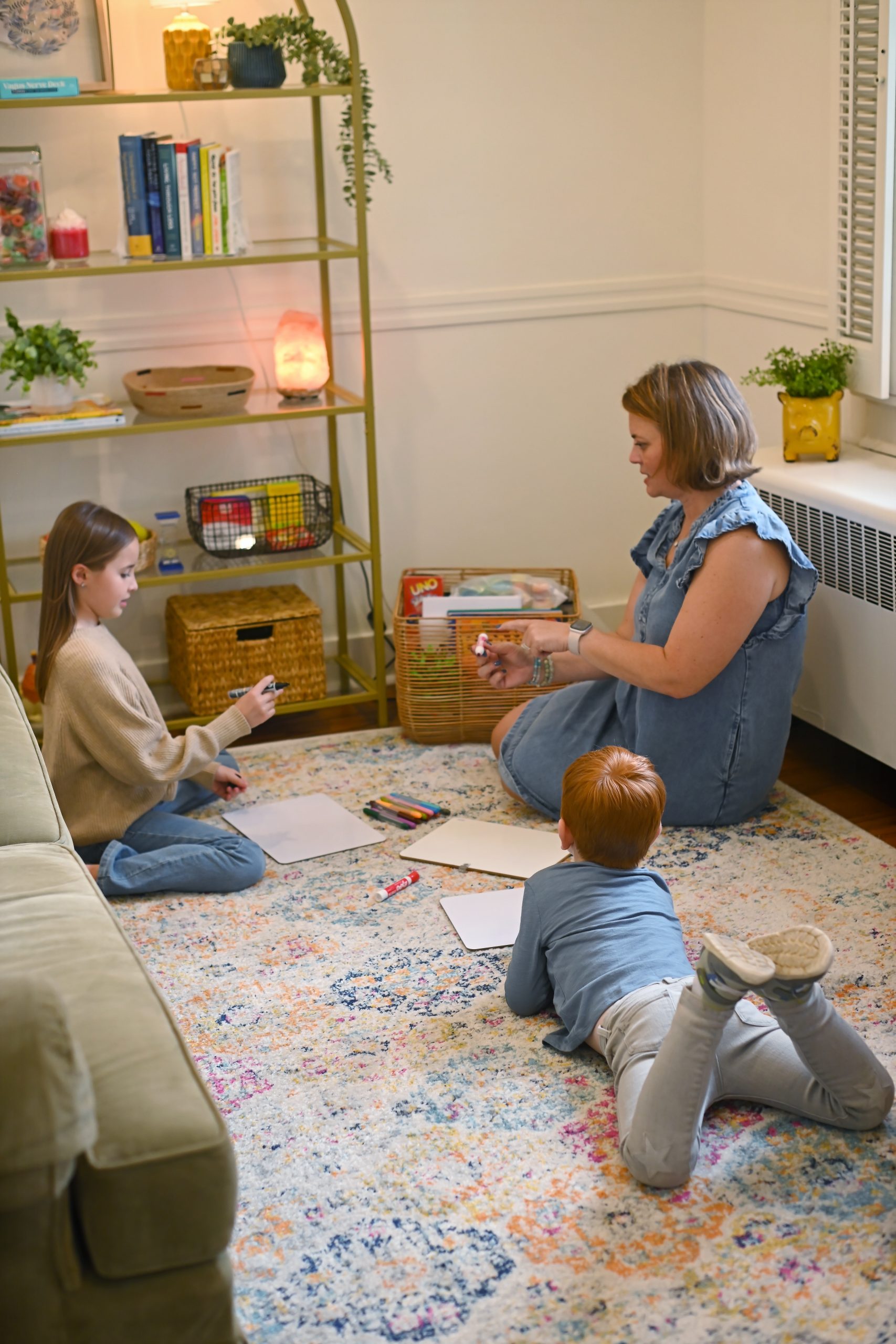 Therapist sitting on the floor with a brother and sister, drawing together during a family session in Troy, Ohio